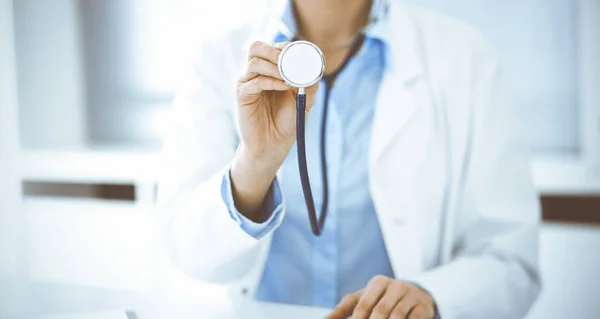 Άγνωστη γυναίκα-γιατρός με μπλε μπλούζα κρατά το κεφάλι στηθοσκοπίου ενώ κάθεται στο γραφείο στην κλινική, κοντινό πλάνο. Γιατρός έτοιμος να εξετάσει και να βοηθήσει ασθενή. Έννοια ιατρικής — Φωτογραφία Αρχείου