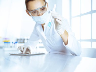 Kadın laboratuvar asistanı mavi sıvıyla test tüpünü analiz ediyor. Tıp, sağlık ve araştırma konsepti