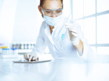 Kadın laboratuvar asistanı mavi sıvıyla test tüpünü analiz ediyor. Tıp, sağlık ve araştırma konsepti