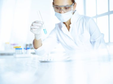 Kadın laboratuvar asistanı mavi sıvıyla test tüpünü analiz ediyor. Tıp, sağlık ve araştırma konsepti