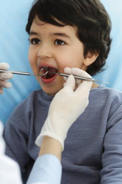 Küçük Arap çocuk dişçi doktoruna sözlü muayene sırasında ağzı açık bir şekilde dişçi koltuğunda oturuyor. Stomatoloji kavramı