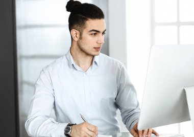 İşadamı modern ofiste bilgisayarla çalışıyor. Arap erkek girişimcinin iş yerindeki portresi. İş konsepti