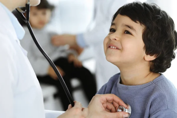 Médico-mujer examinando a un niño paciente por estetoscopio. Lindo chico árabe y su hermano en la cita con el médico. Concepto de medicina —  Fotos de Stock