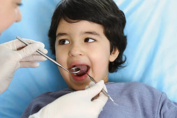 Carino ragazzo arabo seduto sulla sedia dentale con la bocca aperta durante il controllo orale con il medico. Visita studio dentistico. Concetto di stomatologia — Foto Stock