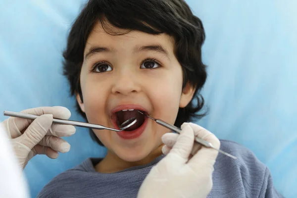 Cute chłopiec arabski siedzi na krześle dentystycznym z otwartymi ustami podczas badania doustnego z lekarzem. Odwiedzam gabinet dentystyczny. Koncepcja stomatologii — Zdjęcie stockowe