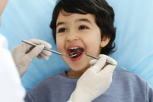 在与医生进行口试时，坐在牙椅上张开嘴的可爱的阿拉伯男孩。去看牙医口腔学概念 — 图库照片