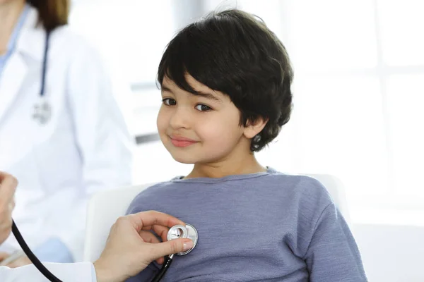 Médico-mujer examinando a un niño paciente por estetoscopio. Lindo chico árabe en la cita con el médico. Concepto de medicina —  Fotos de Stock