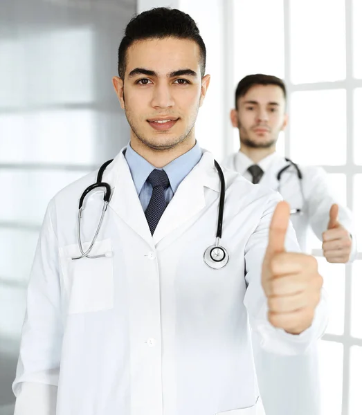 Arabische arts toont OK teken met duimen omhoog met Kaukasische collega in het medisch kantoor of kliniek. Diverse artsen team, beste behandeling, geneeskunde en gezondheidszorg concept — Stockfoto