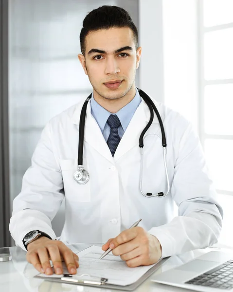 Homem médico árabe está usando computador portátil ao preencher registros de histórico de medicação na mesa de vidro na clínica r. Conceito de medicina — Fotografia de Stock