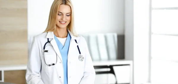 Mujer-médico en el trabajo en la clínica emocionada y feliz de su profesión. Mujer rubia médico está sonriendo mientras se utiliza la tableta. Concepto de medicina — Foto de Stock