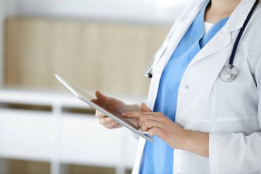 Bilinmeyen kadın doktor klinikte duruyor ve tablet bilgisayar kullanıyor, yakın plan. Tıp ve sağlık alanlarındaki veriler