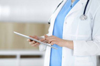 Bilinmeyen kadın doktor klinikte duruyor ve tablet bilgisayar kullanıyor, yakın plan. Tıp ve sağlık alanlarındaki veriler