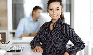 Modern ofisteki işyerinde bilgisayar kullanan bir iş kadını. Esmer sekreter ya da kadın avukat kameraya bakıyor ve mutlu gülümsüyor. Zevk ve başarı için çalışmak