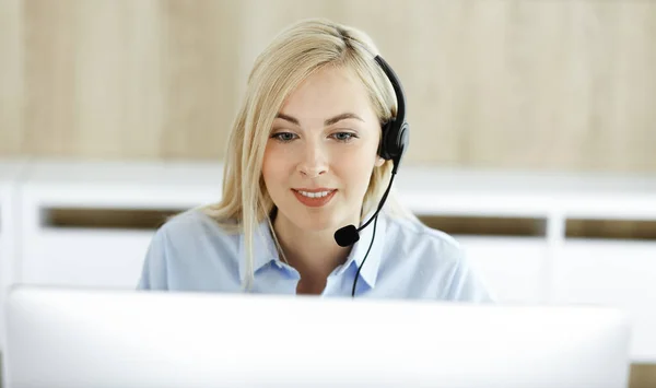 Mujer rubia de negocios sentada y comunicada por auriculares en la oficina del centro de llamadas. Concepto de negocio de telesales u ocupación de oficina en el hogar —  Fotos de Stock