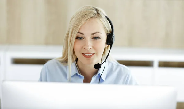 Donna d'affari bionda seduta e comunicata da auricolare in ufficio call center. Concetto di attività di televendita o professione di home office — Foto Stock