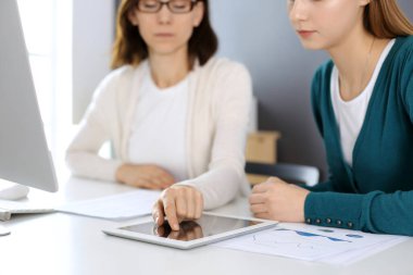 İş kadını, bayan meslektaşına sunum yaparken tablet bilgisayar ekranını işaret ediyor. Ofisteki masada çalışan bir grup iş adamı. Takım çalışması konsepti
