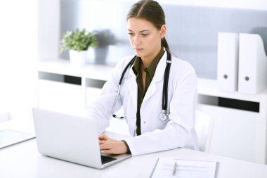 Hastane ofisindeki masada otururken dizüstü bilgisayarda yazan bir doktor. Hekim kadın iş başında. Tıp ve sağlık alanlarındaki veriler