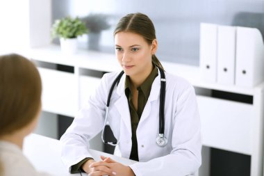 Kadın doktor ve hasta hastane muayenehanesinde oturup konuşuyorlar. Yeşil renkli bluz terapiste yakışır. Tıp ve sağlık hizmetleri kavramı