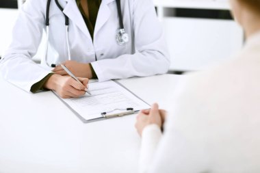Kadın doktor ve hasta hastane muayenehanesinde oturuyor ve konuşuyor, yakın plan. İlaç kayıtlarını dolduran bir terapist. Tıp ve sağlık hizmetleri kavramı
