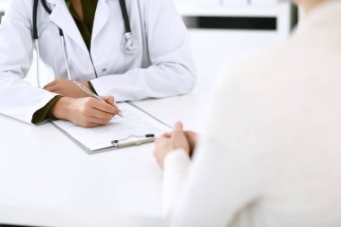 Kadın doktor ve hasta hastane muayenehanesinde oturuyor ve konuşuyor, yakın plan. İlaç kayıtlarını dolduran bir terapist. Tıp ve sağlık hizmetleri kavramı