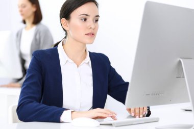 Ofiste bilgisayarla çalışan bir iş kadını, arka planda çalışan bir iş arkadaşı. Masada otururken avukatın ya da muhasebecinin vesikalığı.