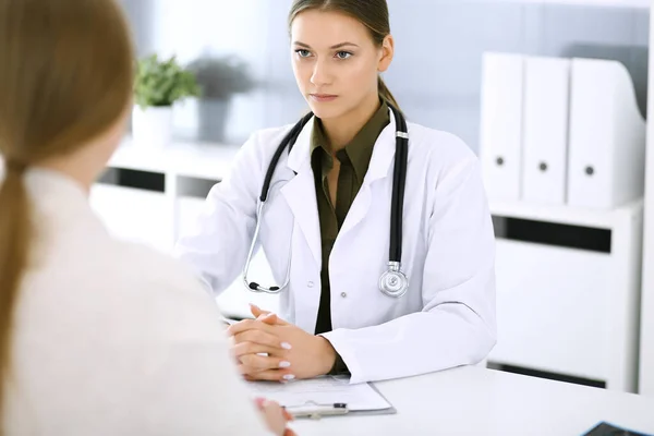 Woman doctor and patient sitting and talking at medical examination at hospital office. Green color blouse suits to therapist. Medicine and healthcare concept — Stock Photo, Image