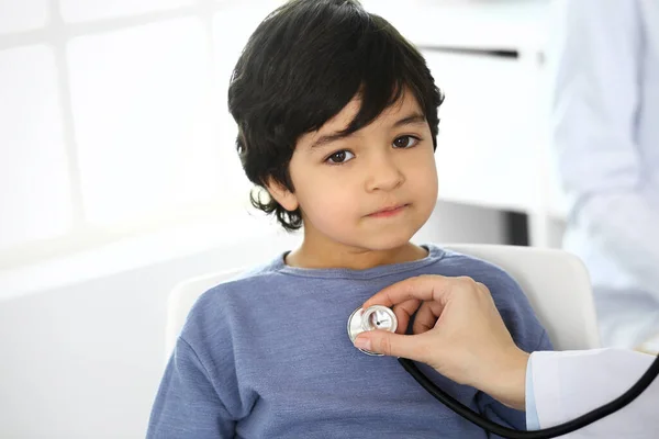 Arzt untersucht eine Kinderpatientin mit einem Stethoskop. Netter arabischer Junge beim Arzttermin. Medizin und Gesundheitskonzept — Stockfoto