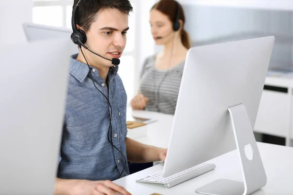 Group of operators at work. Call center. Focus on young man receptionist in headset at customer service. Business concept and casual clothing style — Stock Photo, Image