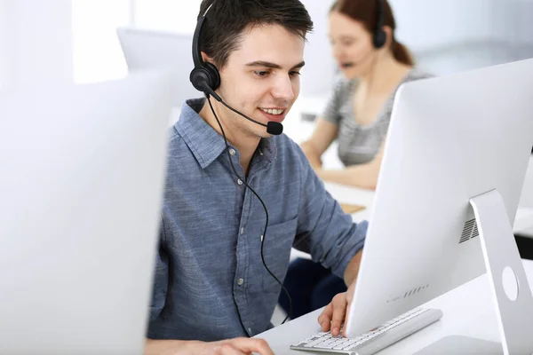 Group of operators at work. Call center. Focus on young man receptionist in headset at customer service. Business concept and casual clothing style — Stock Photo, Image
