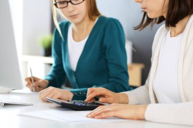 Muhasebeci mali durumu kontrol ediyor ya da vergi formları için hesap makinesi geliri ile sayıyor, eller yakın çekim. İş kadını ofisteki masada iş arkadaşıyla oturuyor ve çalışıyor. Denetim kavramı