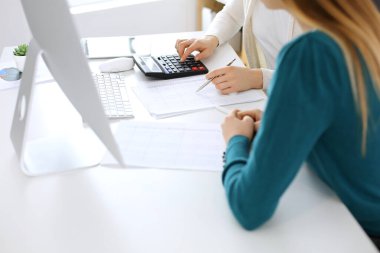 Muhasebeci mali durumu kontrol ediyor ya da vergi formları için hesap makinesi geliri ile sayıyor, eller yakın çekim. İş kadını ofisteki masada iş arkadaşıyla oturuyor ve çalışıyor. Denetim kavramı