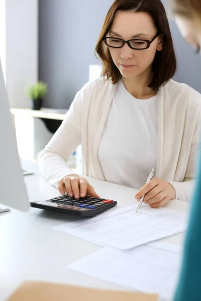 Contabile controllare il bilancio o conteggio dal reddito calcolatrice per la forma fiscale, mani primo piano. Donna d'affari seduta e che lavora con un collega alla scrivania in ufficio. Concetto di audit — Foto Stock