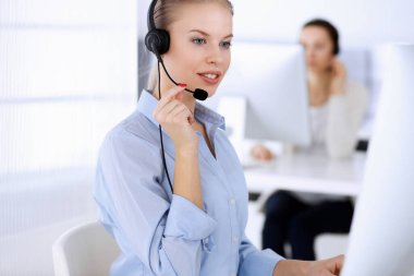 Merkezi ara. İnternette müşterilere danışmak için bilgisayar ve kulaklık kullanan güzel sarışın kadın. Müşteri hizmetleri işgali olarak çalışan bir grup operatör. İş adamları konsepti