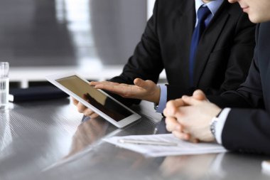 İşadamı tablet bilgisayar kullanıyor ve iş arkadaşı ya da ortağıyla modern ofiste cam masada çalışıyor. Yakın plan. Toplantıda bilinmeyen iş adamları var. Takım çalışması ve ortaklık kavramı