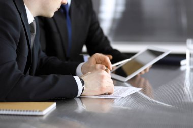 İşadamı tablet bilgisayar kullanıyor ve iş arkadaşı ya da ortağıyla modern ofiste cam masada çalışıyor. Yakın plan. Toplantıda bilinmeyen iş adamları var. Takım çalışması ve ortaklık kavramı