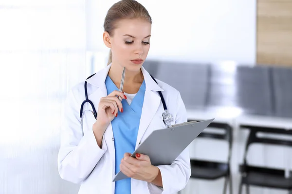 Mulher médica preenchendo registro de histórico de medicação enquanto estava de pé no escritório do hospital de emergência. Médico a trabalhar, retrato de estúdio. Conceito de medicina e cuidados de saúde — Fotografia de Stock