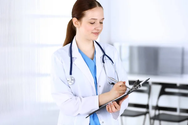 Doctora o estudiante de prácticas en el trabajo. Médico llenando el historial de medicamentos mientras está de pie en la oficina del hospital de emergencia. Concepto de medicina y salud — Foto de Stock