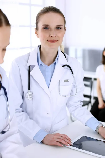 Group of doctors at work in hospital with patient in a queue at the background. Physician filling up medical documents or prescription while standing at reception desk. Data in medicine and health — Stock Photo, Image