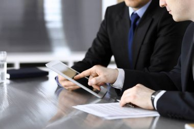 İşadamı tablet bilgisayar kullanıyor ve iş arkadaşı ya da ortağıyla modern ofiste cam masada çalışıyor. Yakın plan. Toplantıda bilinmeyen iş adamları var. Takım çalışması ve ortaklık kavramı
