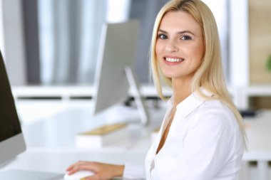 Modern ofisteki işyerinde bilgisayar kullanan bir iş kadını. Sekreter ya da kadın avukat kameraya bakıyor ve mutlu gülümsüyor. Zevk ve başarı için çalışmak