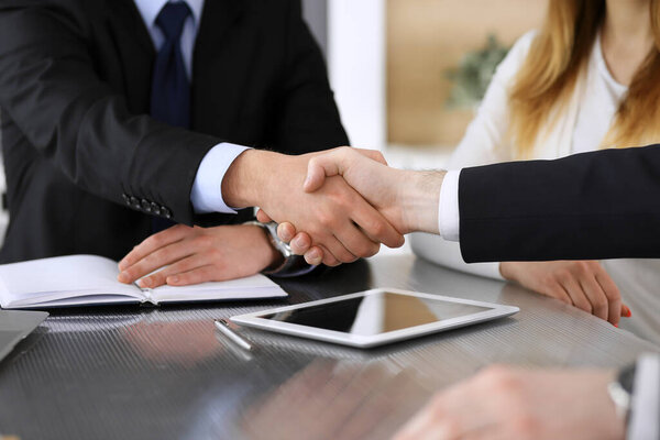 Бизнесмен пожимает руку коллеге или партнеру над стеклянным столом в современном офисе крупным планом. Неизвестные бизнесмены на встрече. Командная работа, партнерство и концепция рукопожатия