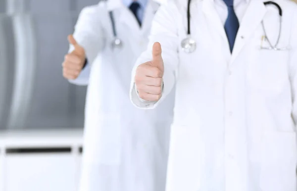 현대 의사들이 한 팀으로 서서 엄지 손가락을 들거나 병원 사무실에서 서류를 클로즈업하는 모습을 볼 수있습니다. 의사들은 환자를 진찰하고 도울 준비가 되어 있다. 의료 지원, 의료 보험, 최상의 치료 — 스톡 사진