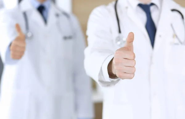 Moderne dokters staan als een team met duimen omhoog of OK tekenen in het ziekenhuiskantoor, close-up. Artsen klaar om patiënten te onderzoeken en te helpen. Medische hulp, verzekering in de gezondheidszorg, beste behandeling — Stockfoto