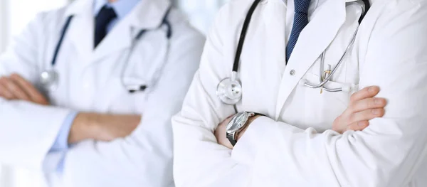 Moderne dokters staan als een team met gekruiste armen in het ziekenhuiskantoor, close-up. Artsen klaar om patiënten te onderzoeken en te helpen. Medische hulp, verzekering in de gezondheidszorg, beste behandeling en — Stockfoto