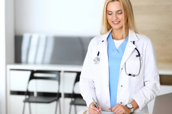 Doctora mujer en el trabajo en el hospital emocionada y feliz de su profesión. Médico rubio controla la historia de la medicación y los resultados del examen. Concepto de medicina y salud — Foto de Stock