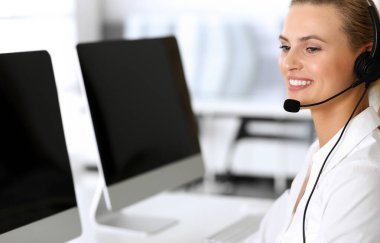 Merkezi ara. İnternette müşterilere danışırken kulaklık kullanan mutlu ve heyecanlı bir iş kadını. Müşteri hizmetleri ofisi ya da tele pazarlama bölümü. İşte gülümseyen sarışın kadın operatör