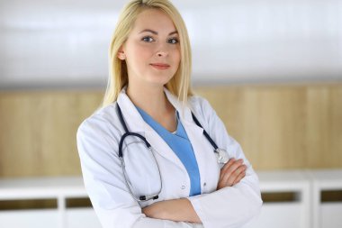 Hastanedeki ya da klinikteki masada oturan doktor kadın. Sarışın, neşeli doktor tıbbi kayıtları dolduruyor. Veriler ve tıp ve sağlık hizmetlerindeki en iyi hizmet