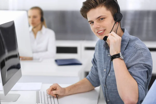 Centro de llamadas. Grupo de operadores vestidos casuales en el trabajo. Enfócate en el joven empresario con auriculares en la oficina de servicio al cliente. Telesales en el negocio —  Fotos de Stock