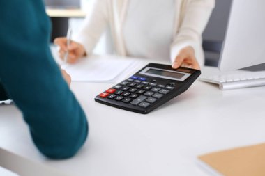 Muhasebeci mali durumu kontrol ediyor ya da vergi formları için hesap makinesi geliri ile sayıyor, eller yakın çekim. İş kadını ofisteki masada iş arkadaşıyla oturuyor ve çalışıyor. Denetim kavramı