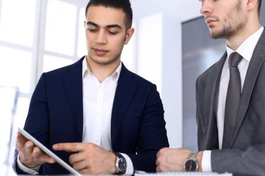 Modern ofisteki masada tablet bilgisayarla çalışan iki iş adamı ya da ortak. İş yerinde iş arkadaşı olan Arap erkek girişimcinin ya da müdürün vesikalığı. Çok ırklı takım çalışması, ortaklık ve